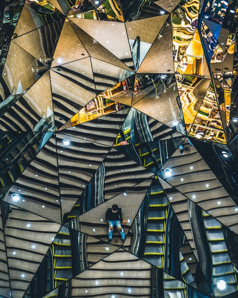 a man sits my staircases reflected by fragments of mirrors above and around him. Accepting a disability has many facets.